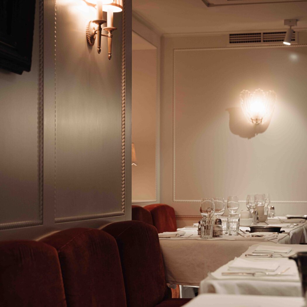 Elegant restaurantinterieur met rode fluwelen banken en witgedekte tafels onder warme wandverlichting.