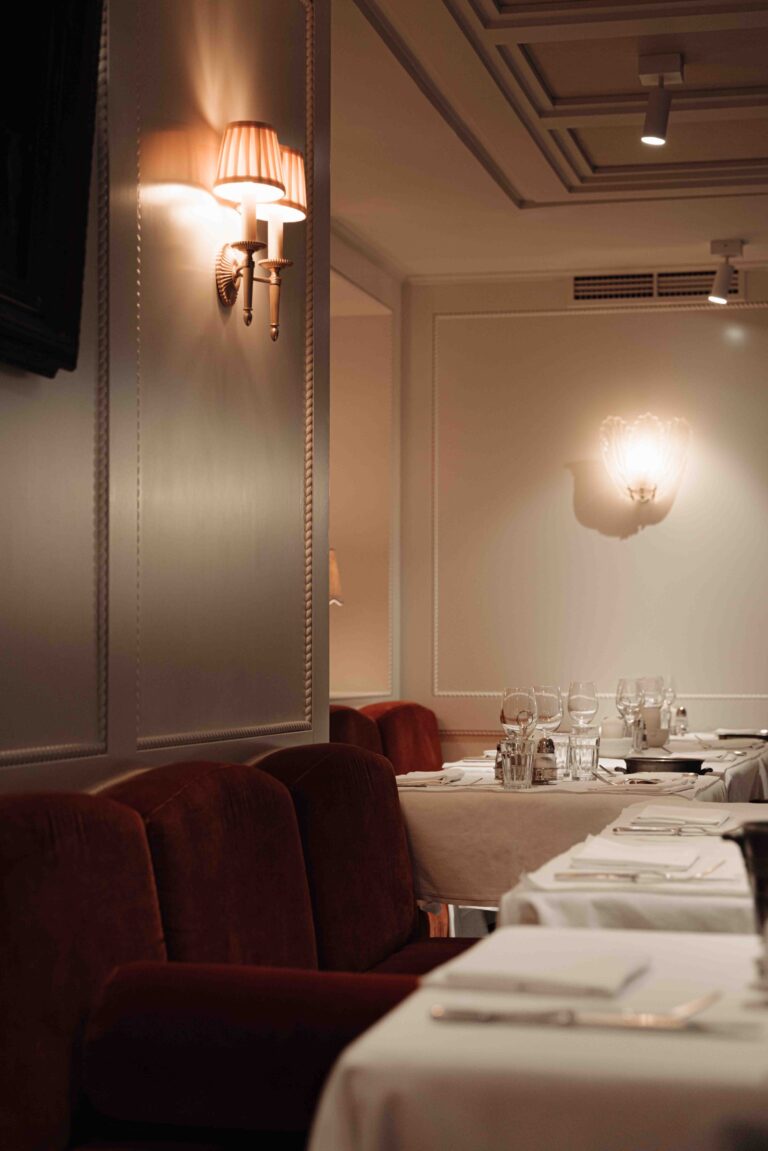 Elegant restaurantinterieur met rode fluwelen banken en witgedekte tafels onder warme wandverlichting.