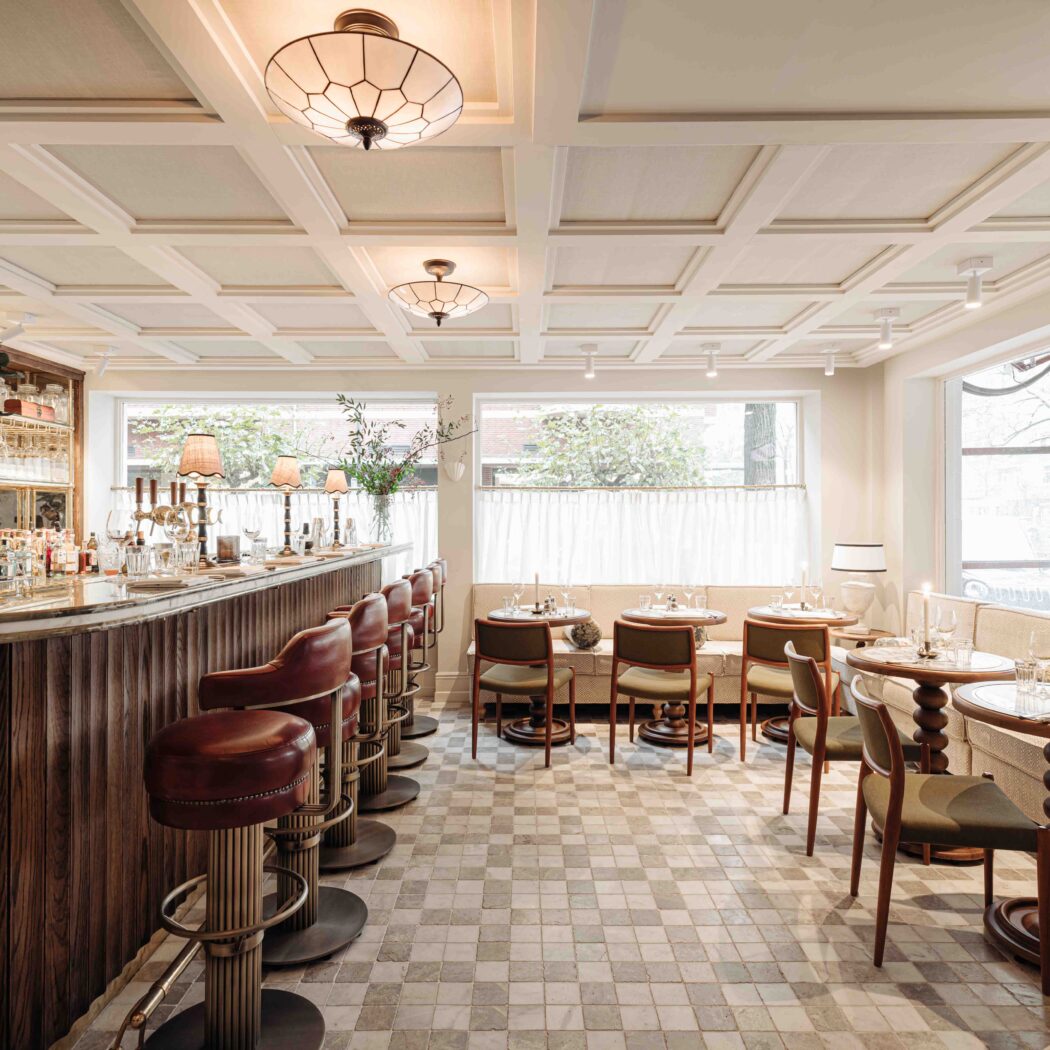 Elegant bar-restaurant interieur met marmeren bar, rode leren barstoelen, tafels en een geruite vloer.