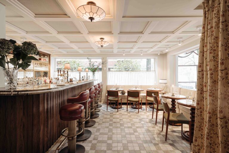 Elegant bar-restaurant interieur met marmeren bar, rode leren barstoelen, tafels en een geruite vloer.
