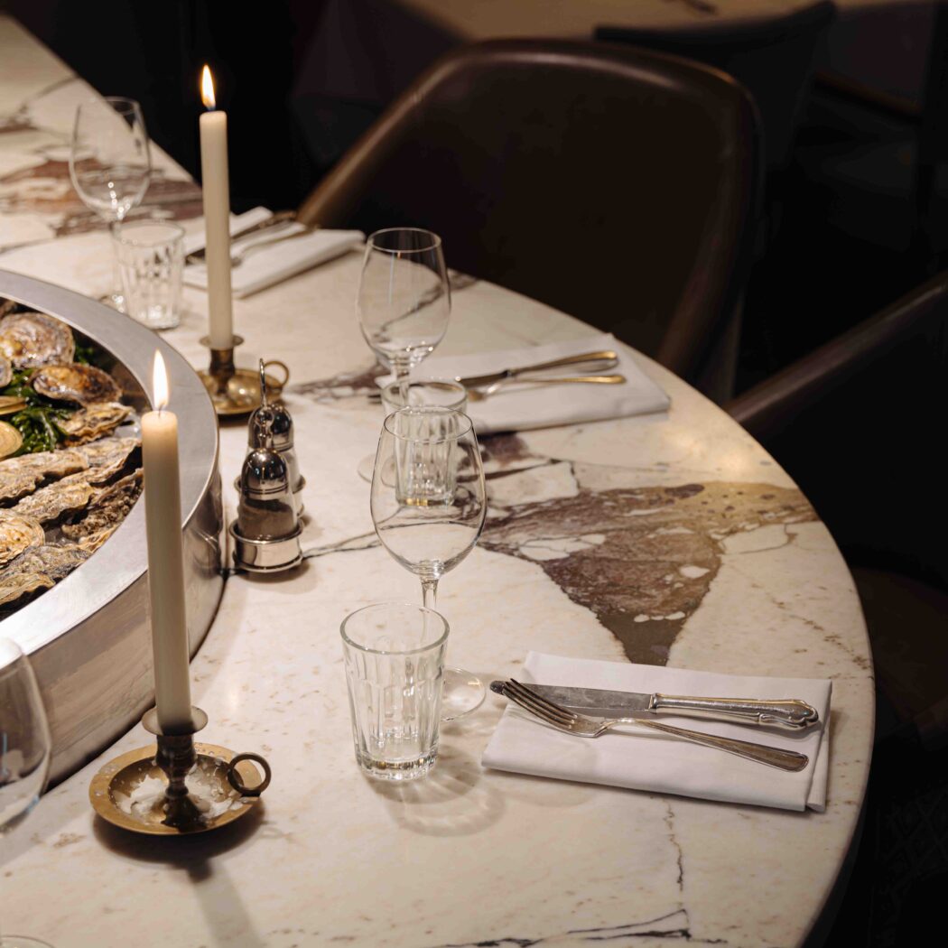 Grote zeevruchtenschotel met oesters op een witte marmeren restauranttafel, sfeervol verlicht door kaarsen.