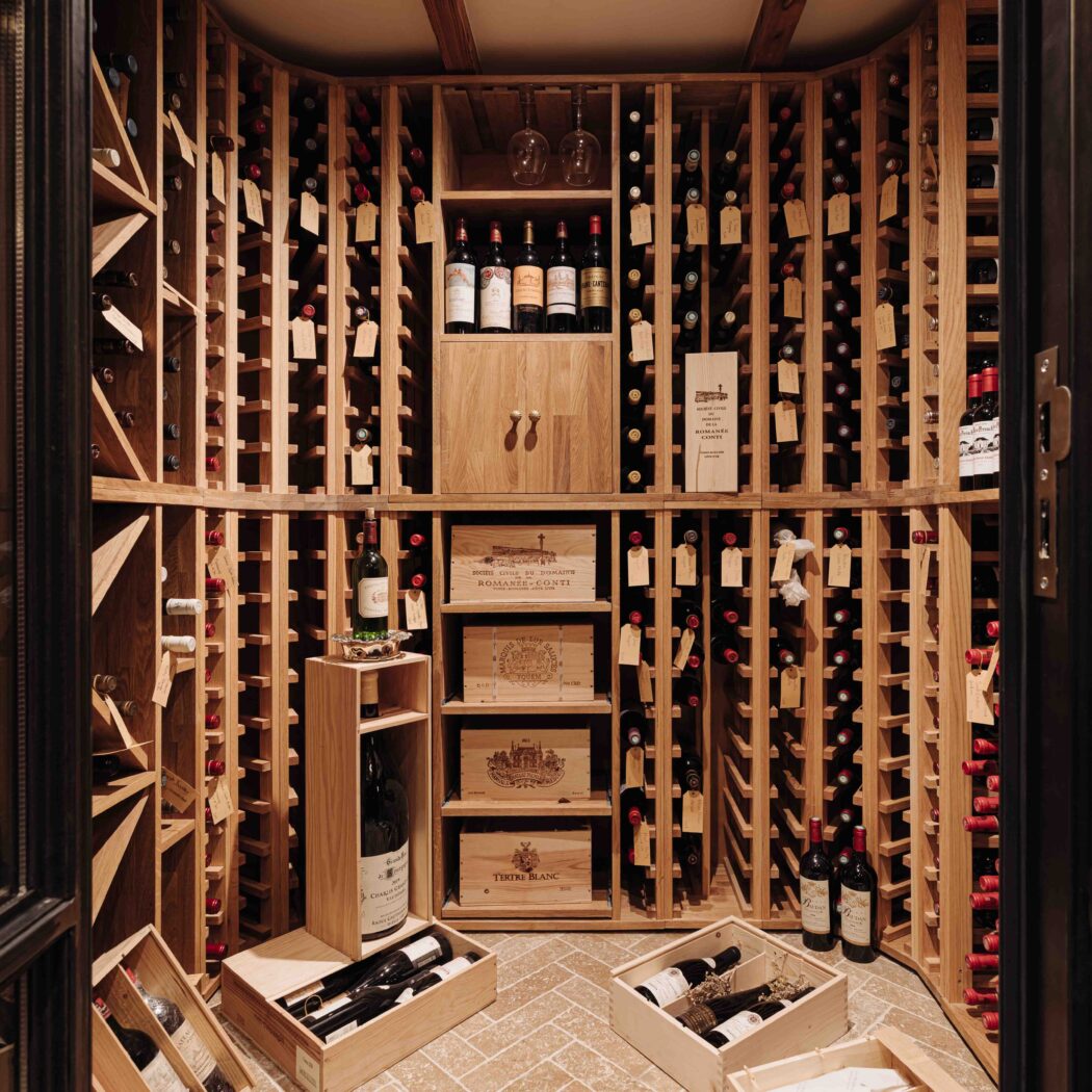 Luxe houten wijnkelder met rijen flessen, Romanee Conti en Titus Blanc wijnkisten, en wijnglazen.