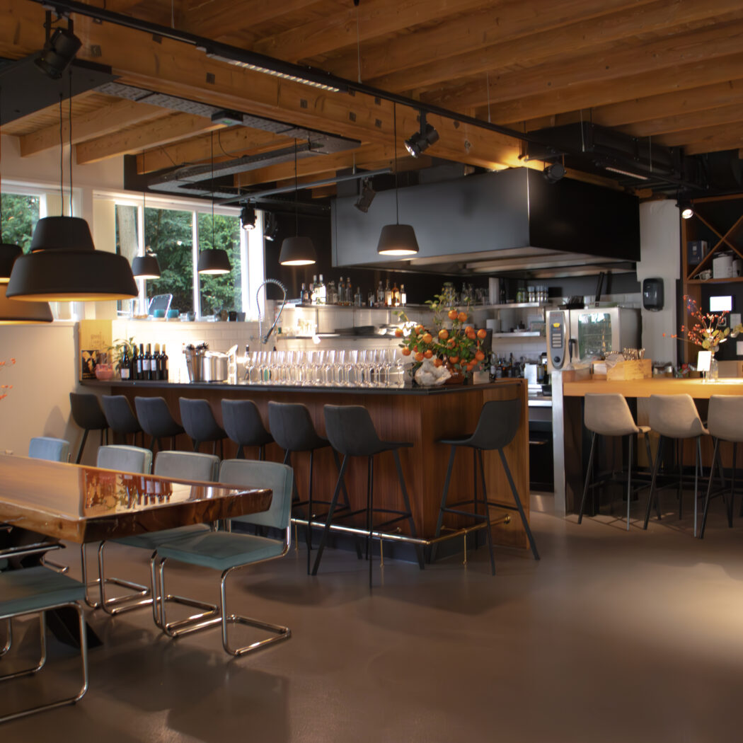 Modern restaurantinterieur met houten tafel, bar, donkere stoelen, balkenplafond en zwarte hanglampen.