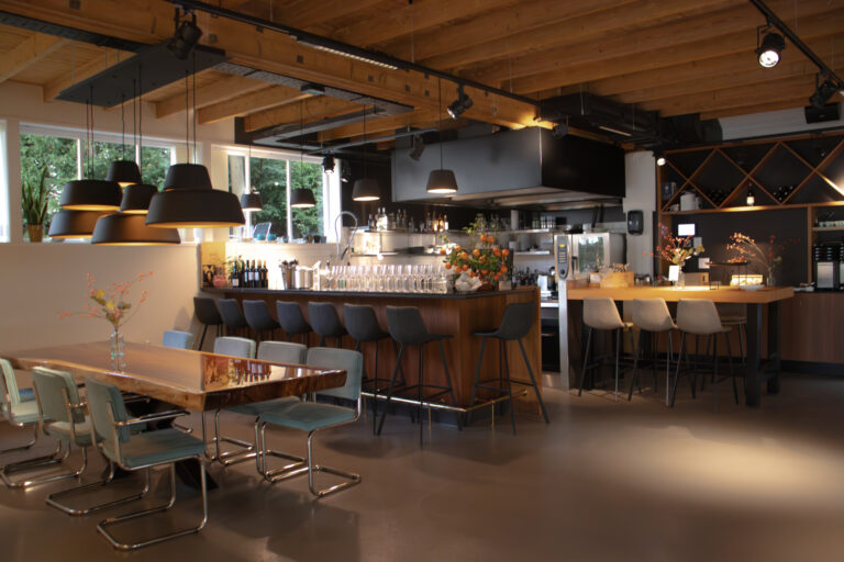 Modern restaurantinterieur met houten tafel, bar, donkere stoelen, balkenplafond en zwarte hanglampen.
