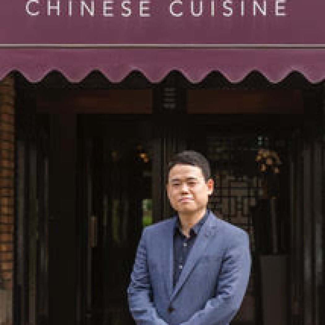 Man in donkerblauw pak staat voor CHANG-i CHINESE CUISINE met bordeauxrode luifel.