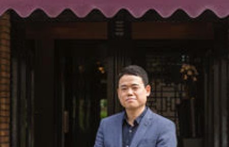 Man in donkerblauw pak staat voor CHANG-i CHINESE CUISINE met bordeauxrode luifel.