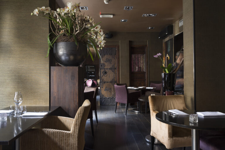 Elegant restaurantinterieur met gedekte tafels, fluwelen stoelen, een grote pot met witte orchideeën en traditionele houten deuren.