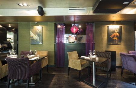 Restaurant interieur met gedekte tafels, paarse en gouden stoelen, en oosterse kunst aan groene wanden.