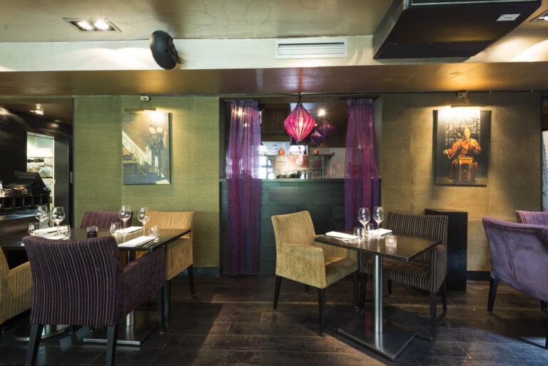 Restaurant interieur met gedekte tafels, paarse en gouden stoelen, en oosterse kunst aan groene wanden.