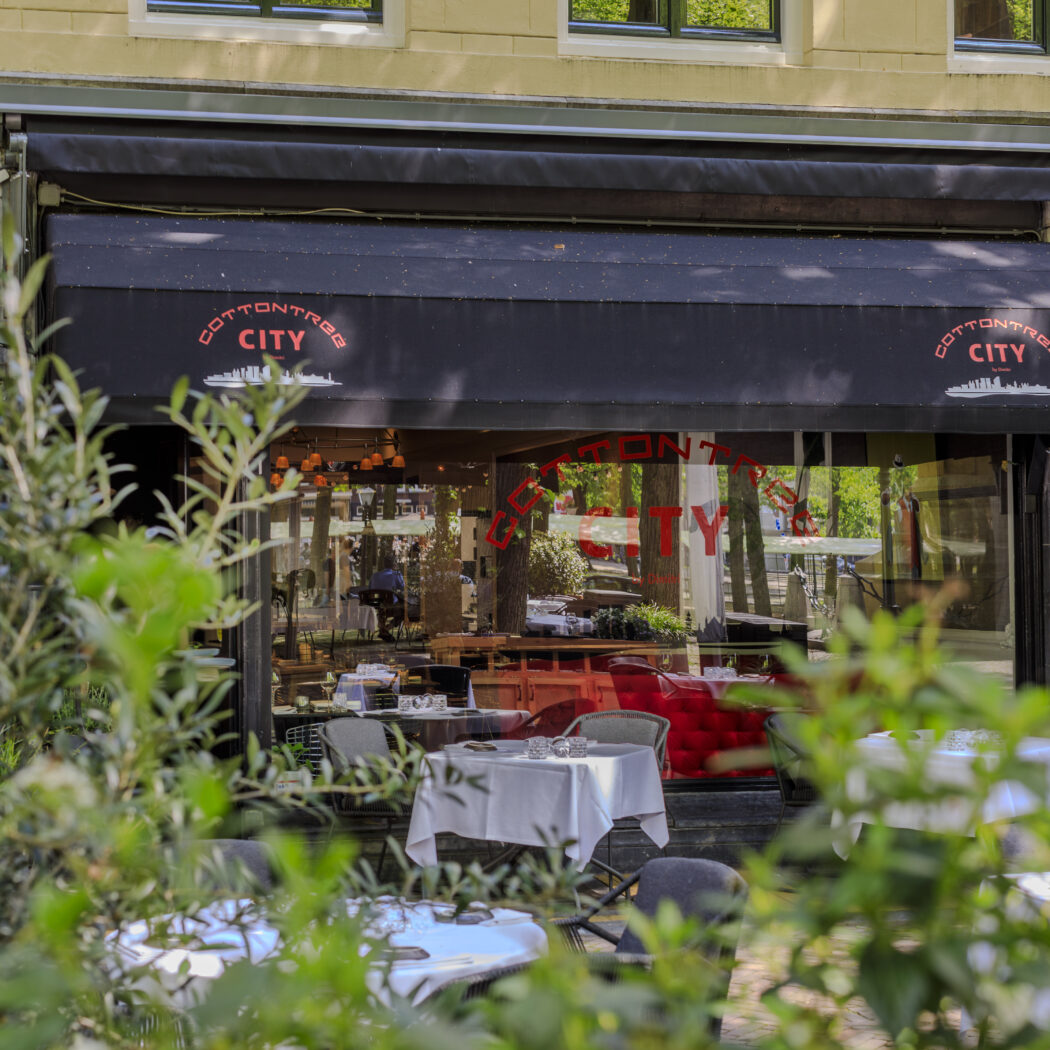 Restaurant Cottontree City met zwart zonnescherm, glazen pui en terrastafels tussen groen.