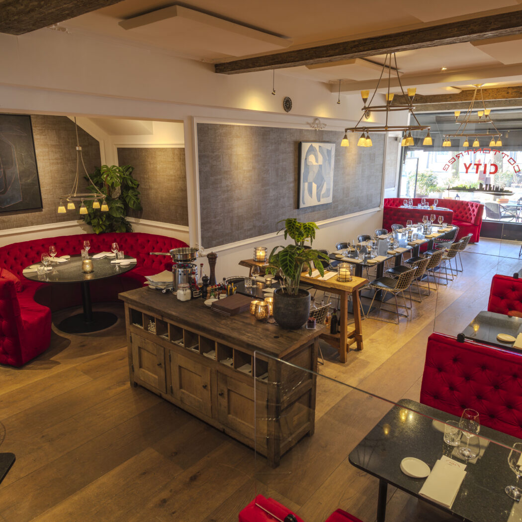 Sfeervol restaurant interieur met rode banken, zwarte tafels en een houten vloer, CITY zichtbaar op het raam.