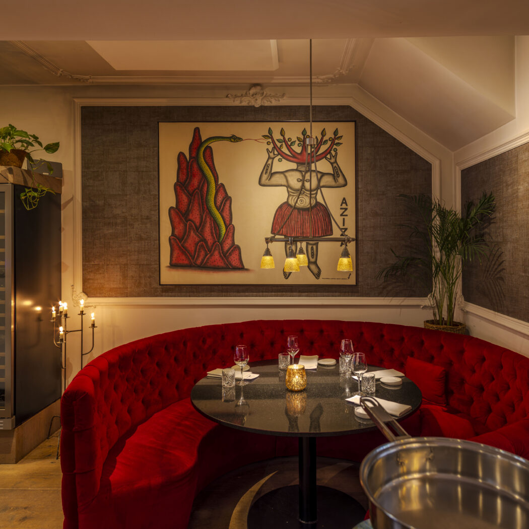 Ronde rode fluwelen bank in een restaurant met gedekte tafel, wijnkoelers en een kunstwerk van een figuur en slang.