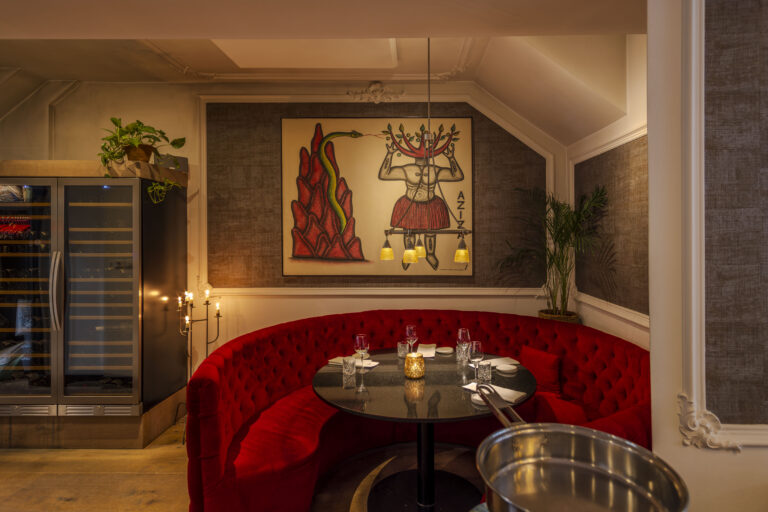Ronde rode fluwelen bank in een restaurant met gedekte tafel, wijnkoelers en een kunstwerk van een figuur en slang.