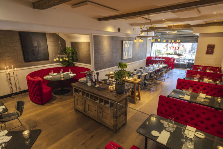 Sfeervol restaurant interieur met rode banken, zwarte tafels en een houten vloer, CITY zichtbaar op het raam.