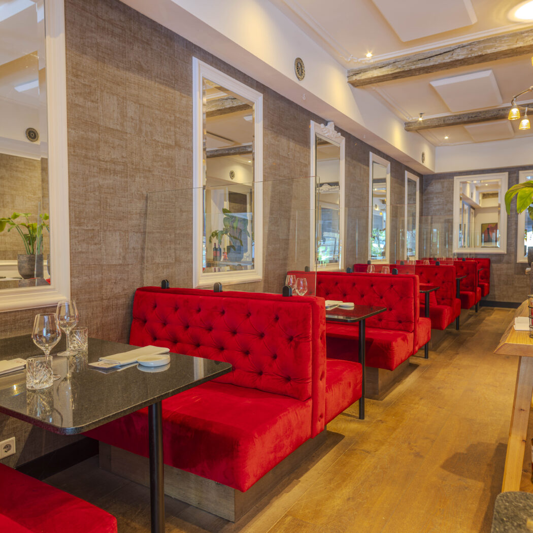Interieur van een restaurant met rode fluwelen banken, zwarte tafels, wandspiegels en houten vloer.