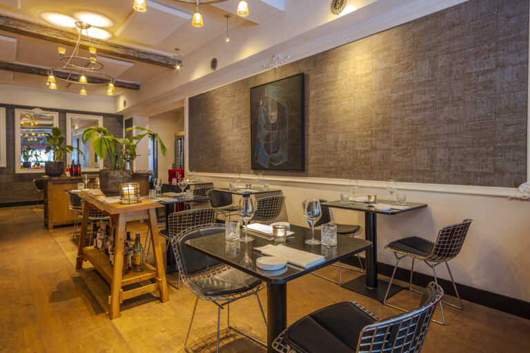 Sfeervol restaurantinterieur met zwarte granieten tafels, draadstoelen, houten vloer, planten en abstracte kunst.