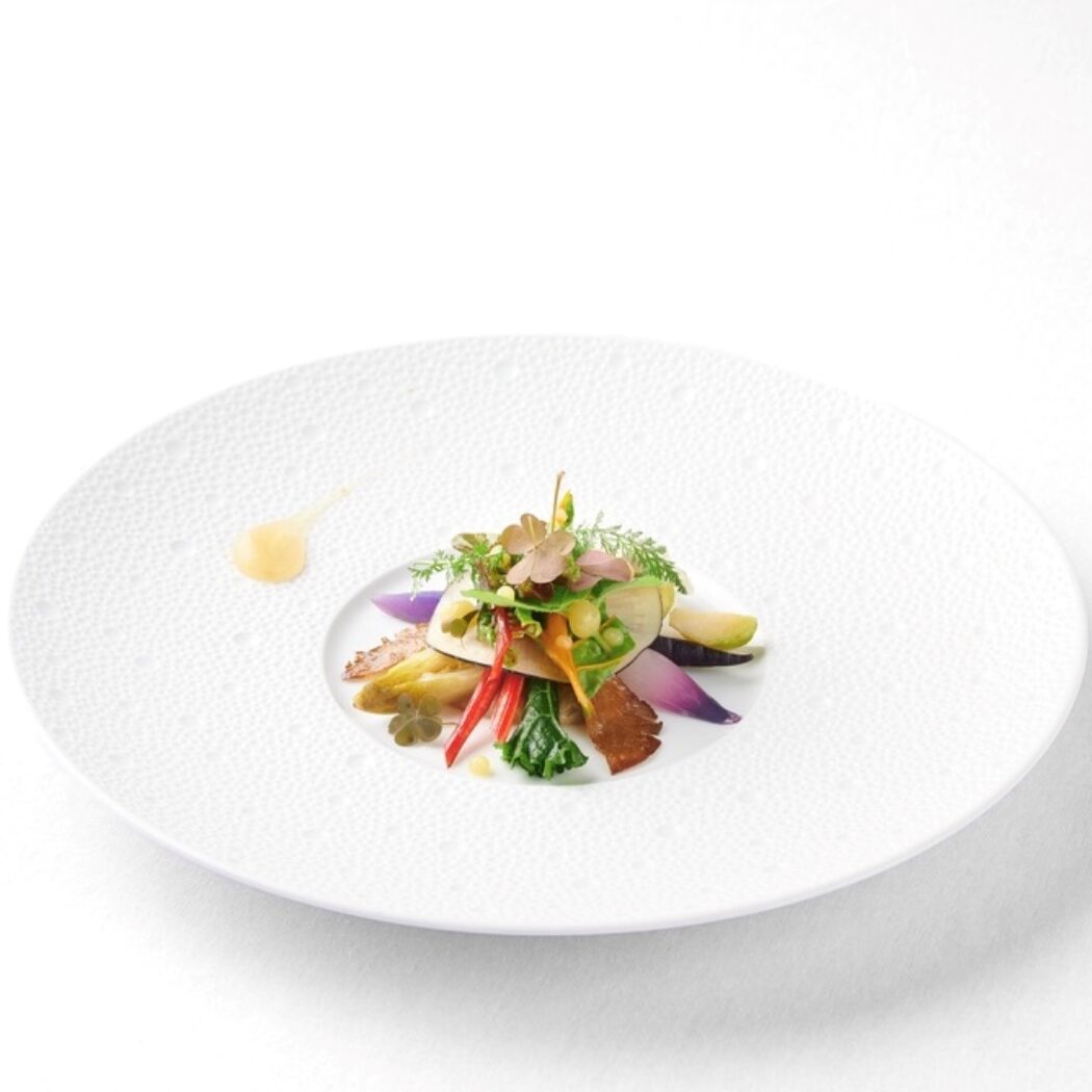Verfijnd gerecht met kleurrijke groenten, microgreens en bloemen, artistiek gepresenteerd op een wit designbord met saus.