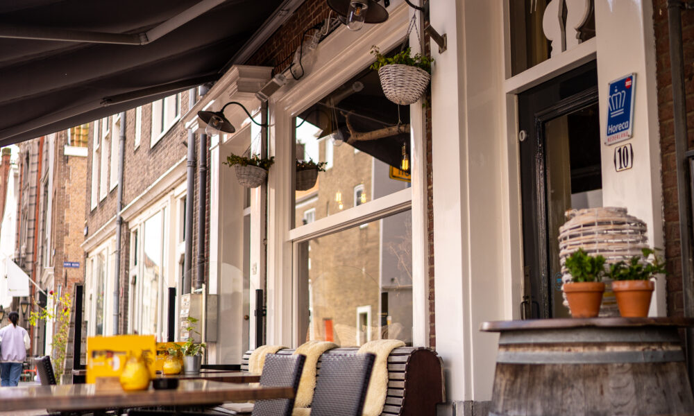 Gezellig buitenterras met zwarte zonneschermen, rieten stoelen met dekens en een Horeca Nederland-keurmerk.
