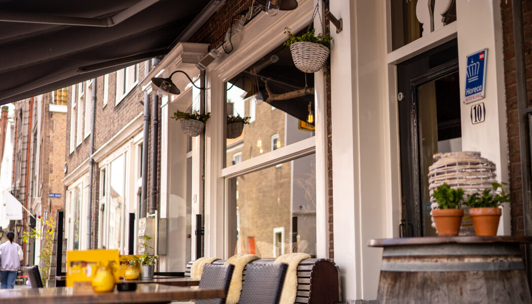 Gezellig buitenterras met zwarte zonneschermen, rieten stoelen met dekens en een Horeca Nederland-keurmerk.
