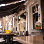 Gezellig buitenterras met zwarte zonneschermen, rieten stoelen met dekens en een Horeca Nederland-keurmerk.