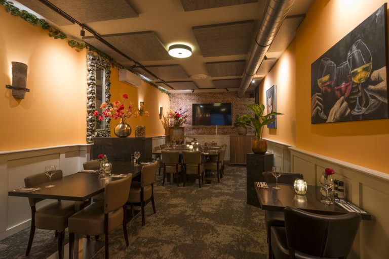 Sfeervol restaurantinterieur met warm oranje muren, gedekte eettafels, bloemstukken en kunst aan de muur.