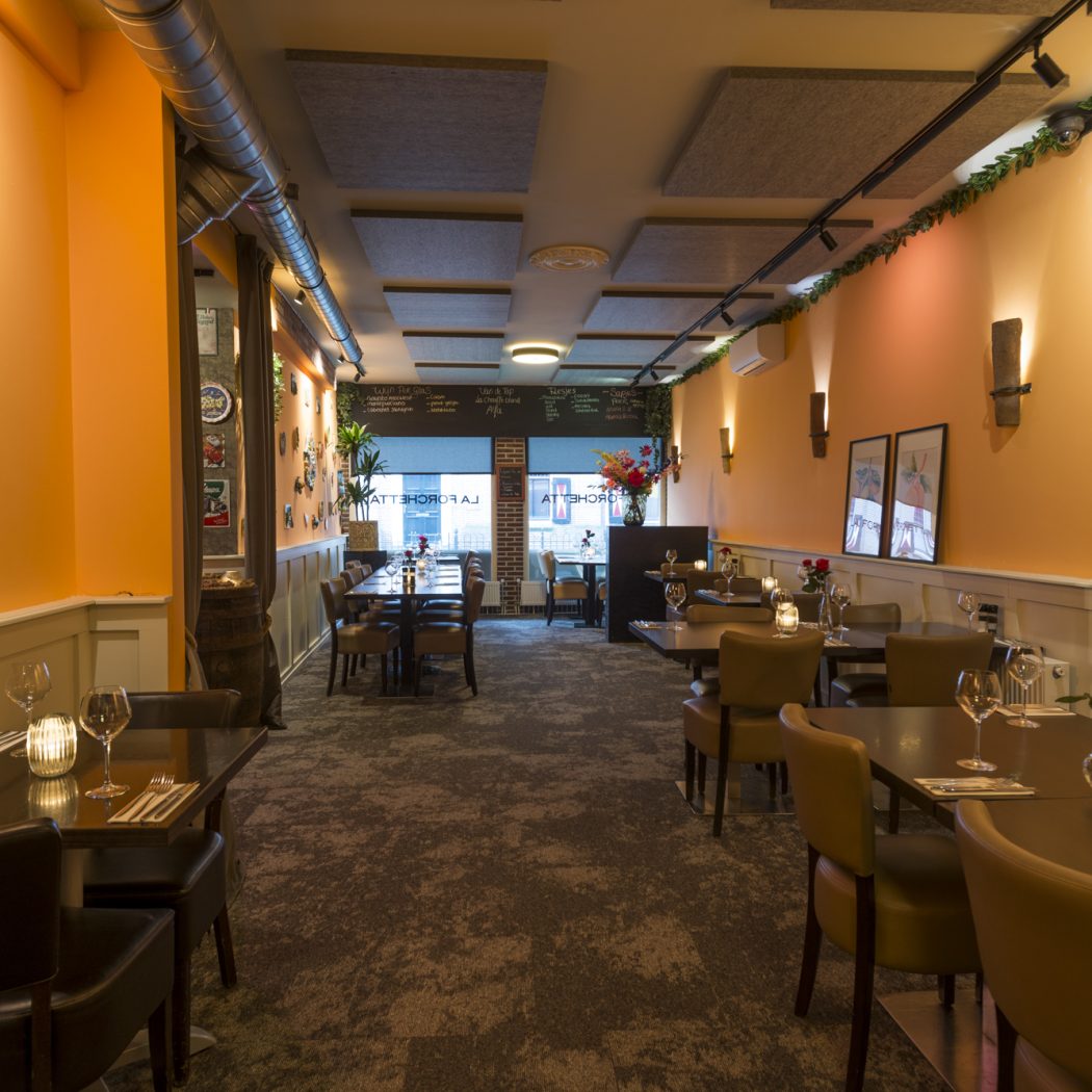 Sfeervol restaurant interieur van La Forchetta met oranje muren, gedekte tafels en warme verlichting.