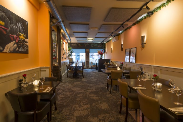 Sfeervol restaurant interieur van La Forchetta met oranje muren, gedekte tafels en warme verlichting.