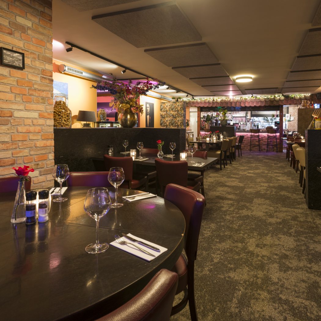 Sfeervol restaurant met gedekte tafels, bakstenen muur met Rome-afbeeldingen en een verlichte bar achterin.
