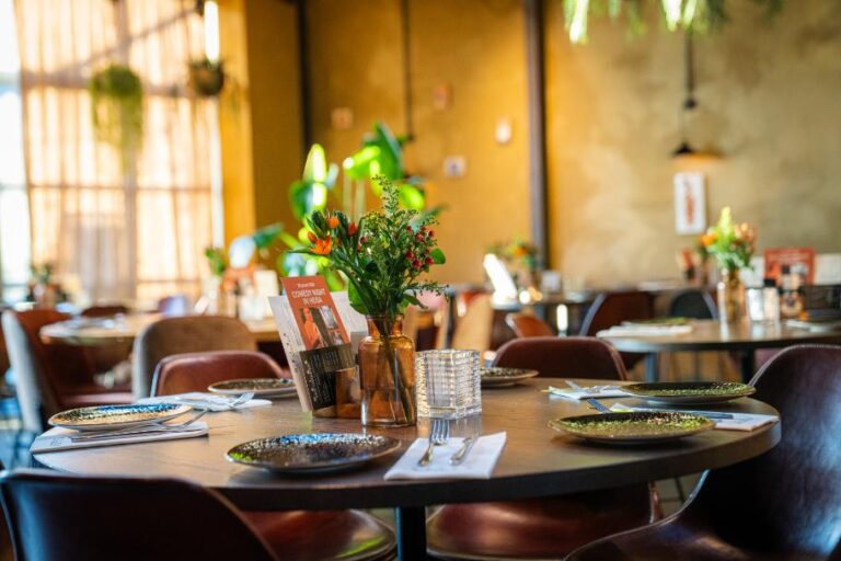 Sfeervolle restauranttafel gedekt met donkere borden, bestek, oranje bloemen en een COMEDY NIGHT flyer.