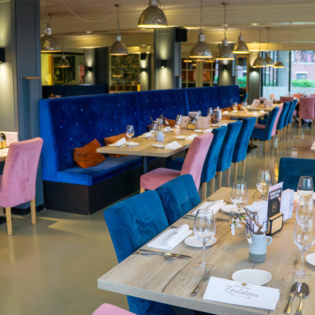Modern restaurant met gedekte houten tafels, blauwe en roze fluwelen zitplaatsen, en menukaarten met Zoutsteen logo.