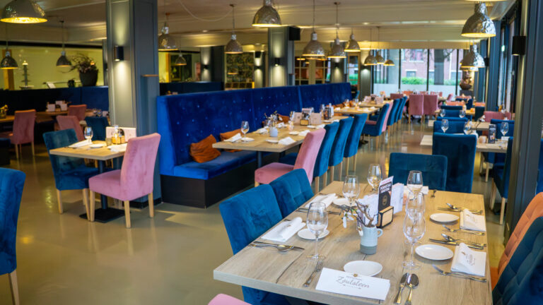 Modern restaurant met gedekte houten tafels, blauwe en roze fluwelen zitplaatsen, en menukaarten met Zoutsteen logo.