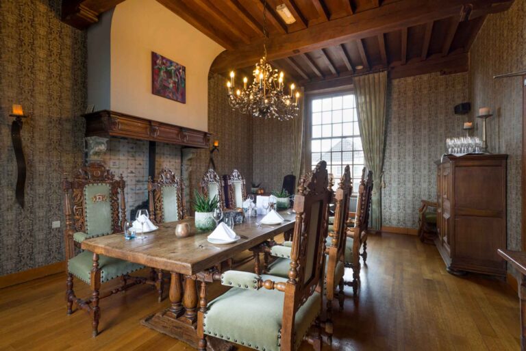 Statige eetzaal met lange houten tafel, sierlijke groene stoelen, kroonluchter en traditionele open haard.