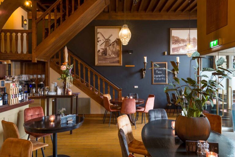 Sfeervol restaurant met houten trap, donkere muur, tafels, diverse stoelen, bar en menu op een krijtbord.