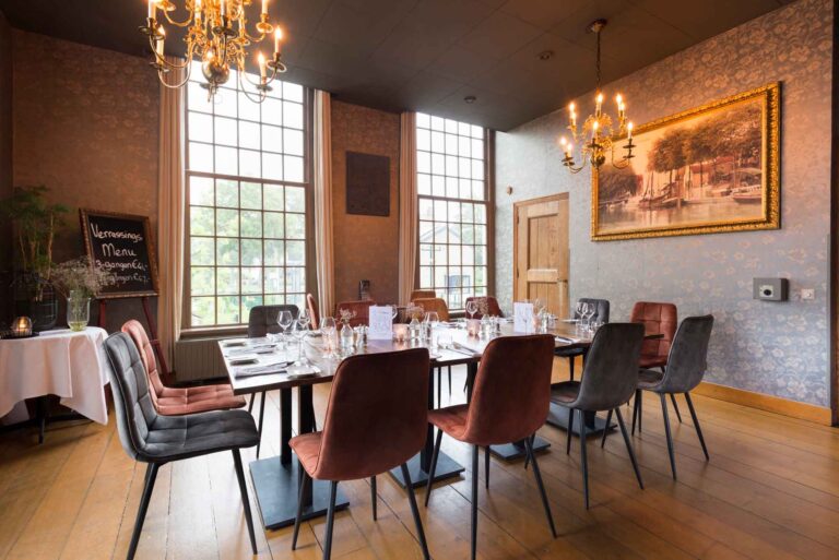Sfeervolle eetzaal met gedekte tafel, gemêleerde stoelen, grote ramen, kroonluchters en krijtbord Verrassings Menu.