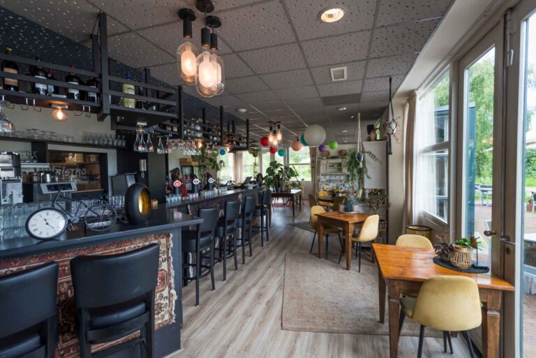 Sfeervol bistro interieur met lange bar, wijnen, houten tafels met gele stoelen en grote ramen. Tekst BISTRO zichtbaar.