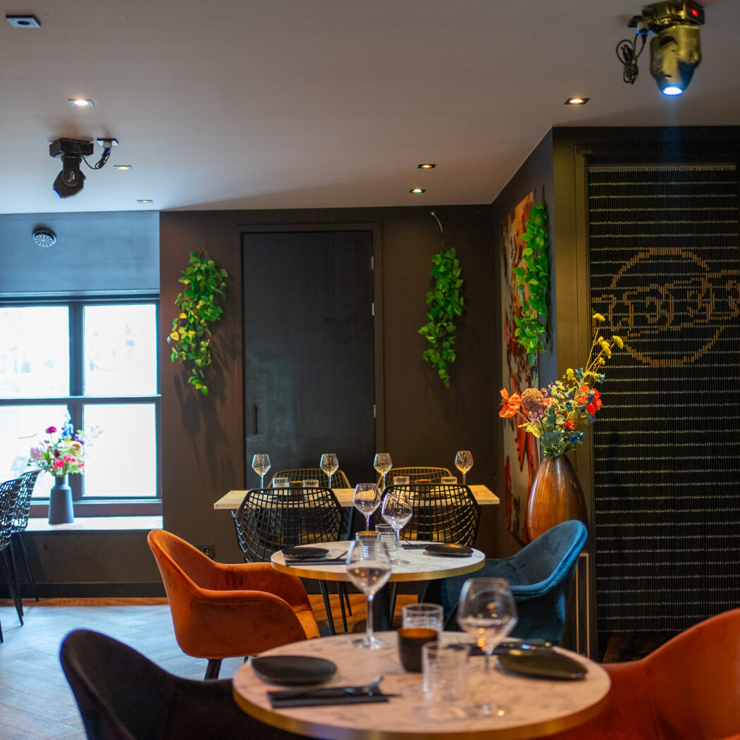 Modern restaurantinterieur met gedekte marmeren tafels, oranje en zwarte stoelen, en een RASA-decorwand.