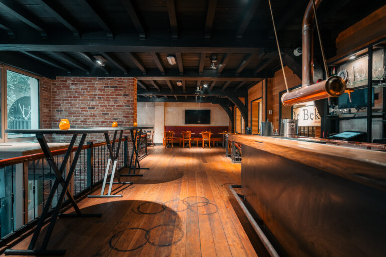 Warm interieur van café De Bek met lange houten bar, koperen biertap, hoge tafels en zithoek.