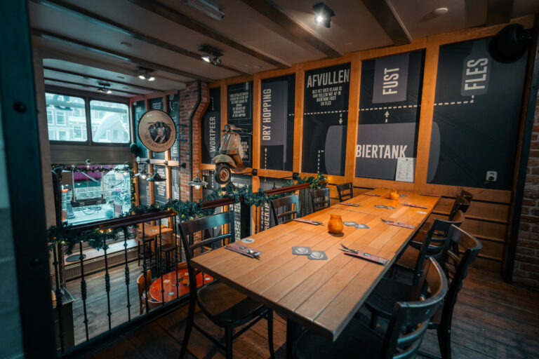 Sfeervol interieur van een brouwerij-pub met lange houten tafel, scooter aan de wand, en muurpanelen over BIERTANK.