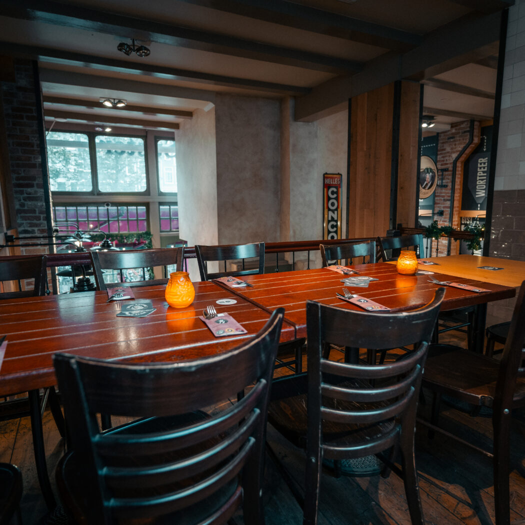 Sfeervol restaurantinterieur met lange houten tafel, gedekte plaatsen, oranje kaarslicht en BELLES CONGO reclamebord.