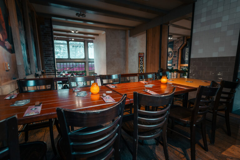 Sfeervol restaurantinterieur met lange houten tafel, gedekte plaatsen, oranje kaarslicht en BELLES CONGO reclamebord.