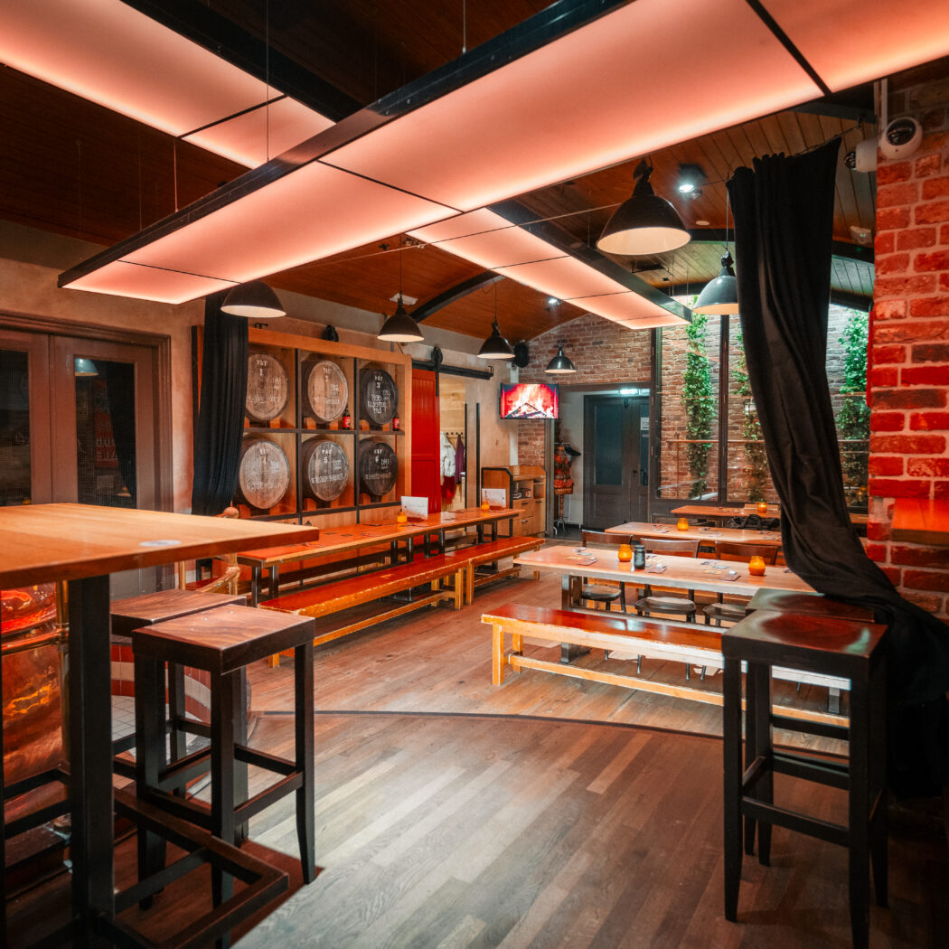 Sfeervol brouwerij restaurant interieur met koperen ketels, houten vaten, hoge tafels en banken onder warme verlichting.