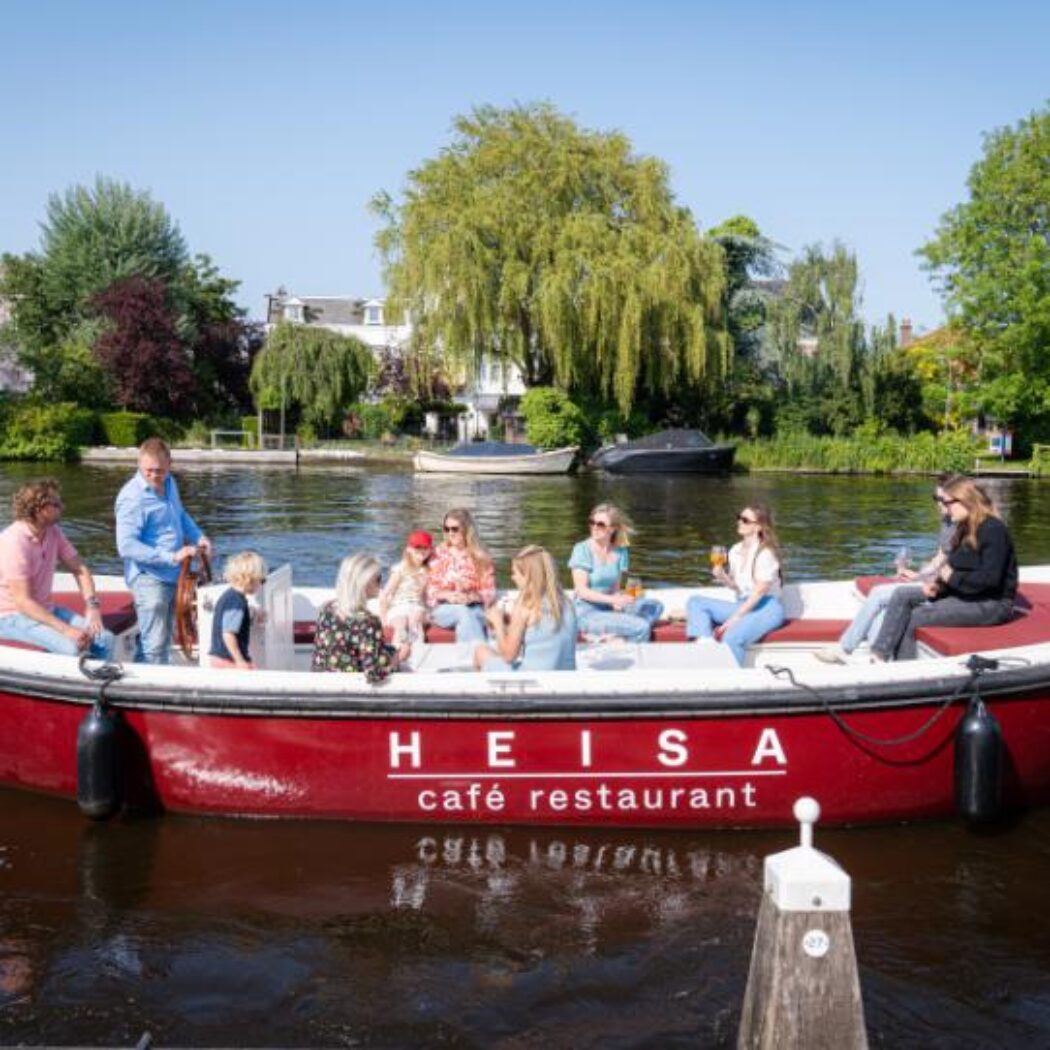Mensen varen ontspannen in een rode HEISA café restaurant sloep op zonnig water.