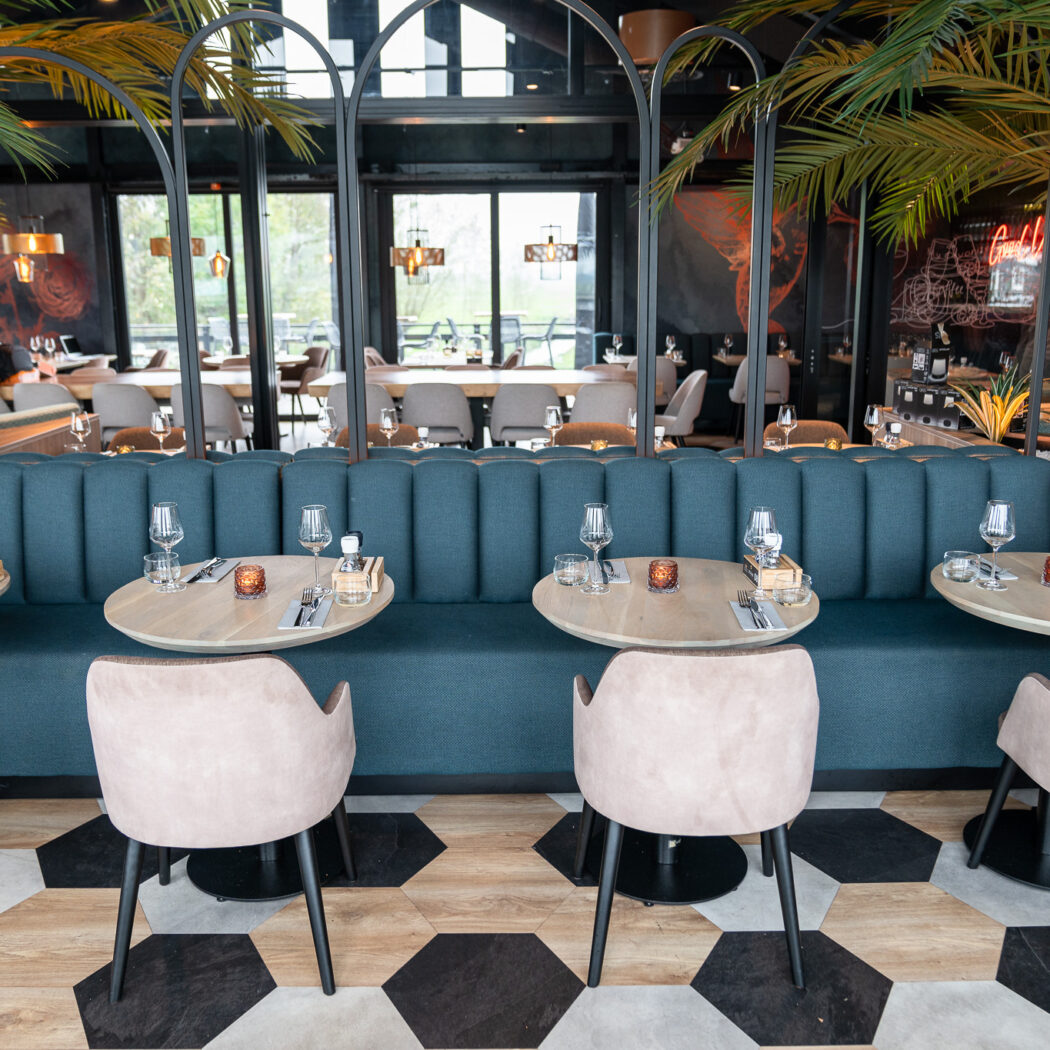 Moderne eetzaal met blauwgroene banken, houten tafels, beige stoelen, palmbomen en Cocktails neon.