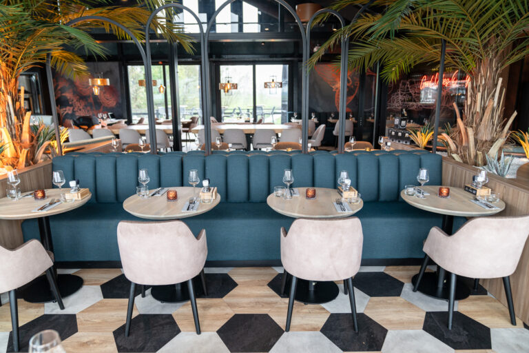 Moderne eetzaal met blauwgroene banken, houten tafels, beige stoelen, palmbomen en Cocktails neon.