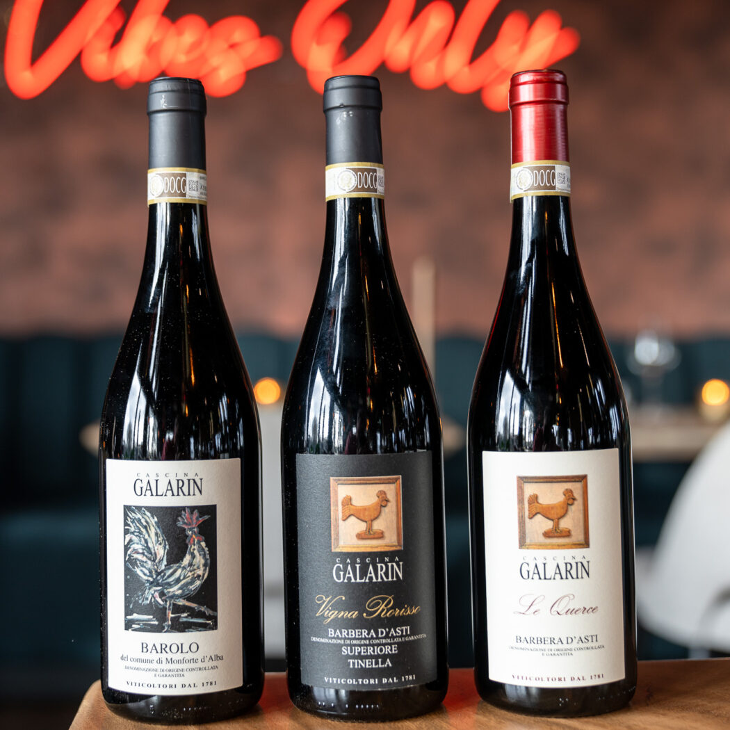 Drie flessen Cascina Galarin rode wijn: Barolo en Barbera dAsti, met haanillustraties op de etiketten.