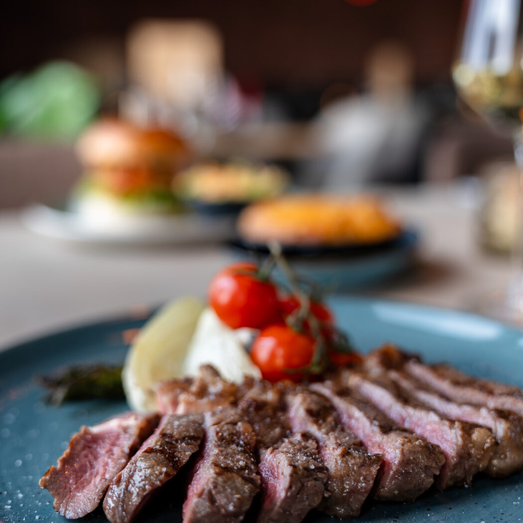 Gesneden medium-rare biefstuk bestrooid met zout, geserveerd met kersentomaten en asperges op een blauw bord.