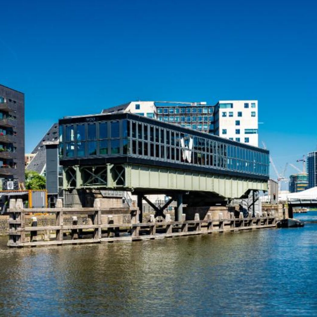 Stadskanaal met verhoogd glazen gebouw WOLF, donkere appartementen en hoge toren met uitkijkplatform.
