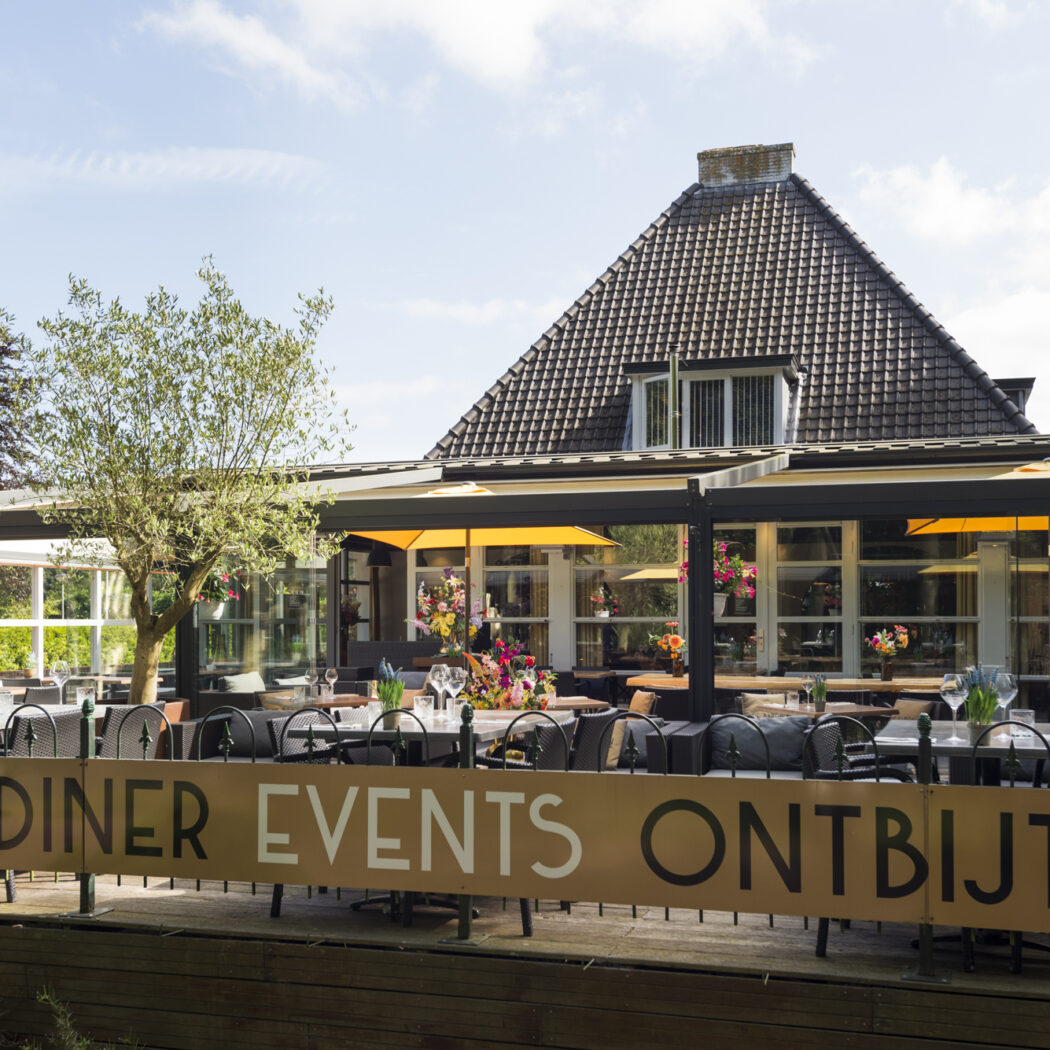 Zonnig buitenterras van een restaurant met glazen overkapping, tafels, bloemen en een banner: Diner Events Ontbijt.