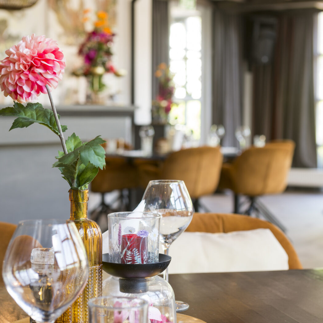Gedekte tafel met roze dahlia, wijnglazen en kaars in een warm restaurant.