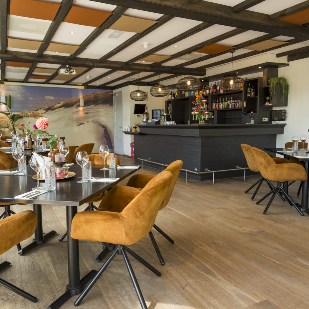 Sfeervol restaurant en bar met gedekte tafels, okergele stoelen en een muurschildering van zandduinen.